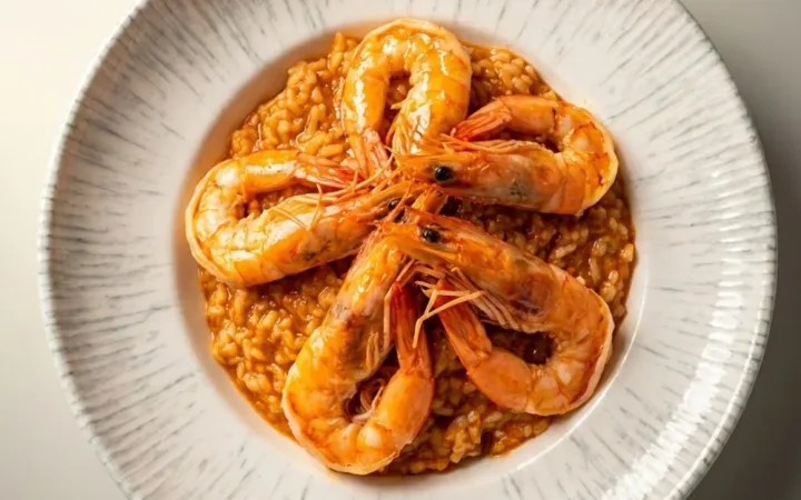 Risotto cu creveți întregi într-o farfurie albă texturată, pe fundal neutru